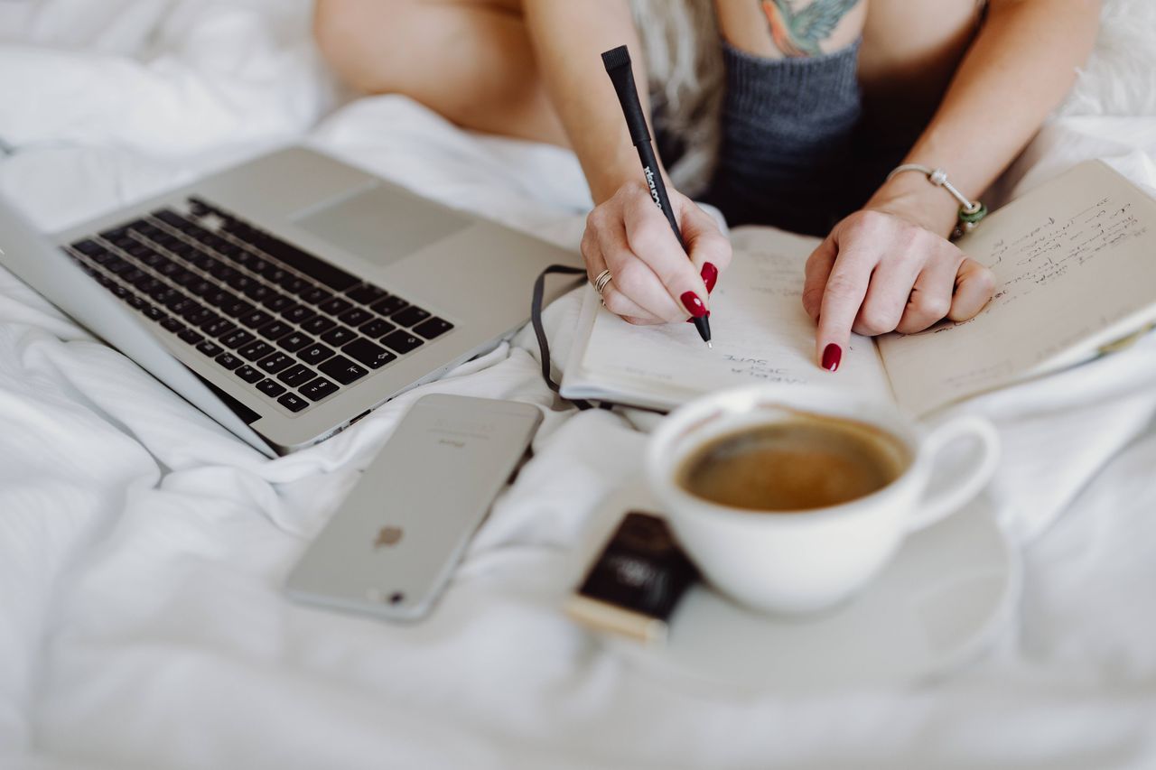 Woman working on a laptop while enjoying a breakfast coffee and chocolate in bed